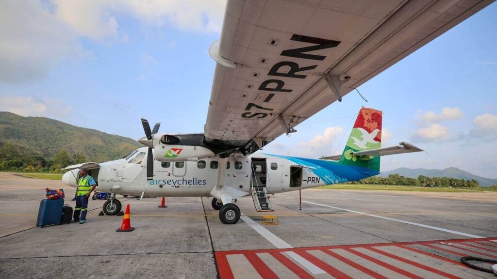 Et fly fra Air Seychelles på rullebanen på øya Praslin på Seychellene. Flyets hale har farger fra naturen og bak flyet skimtes den grønne vegetasjonen. ,