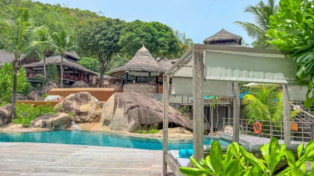 Luksusresort i tradisjonell stil omgitt av tropisk vegetasjon. Solsenger og solterrasse i front av hotellet alt i duse og behagelige farger.