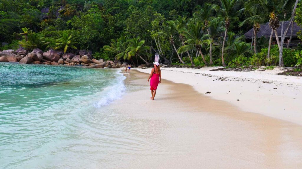 Kvinne i rosa på stranden foran resorten på Seychellene