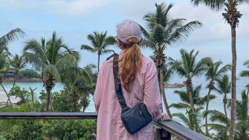 Kvinne kledd i rosa ser ut over eksotiske omgivelser med palmer og strand. 