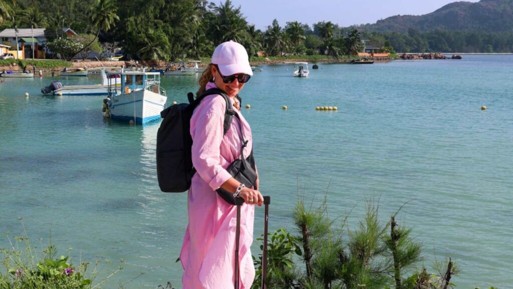 Kvinne med rosa kabinkoffert, sort ryggsekk og crossbody bag p&aring; Seychellene.