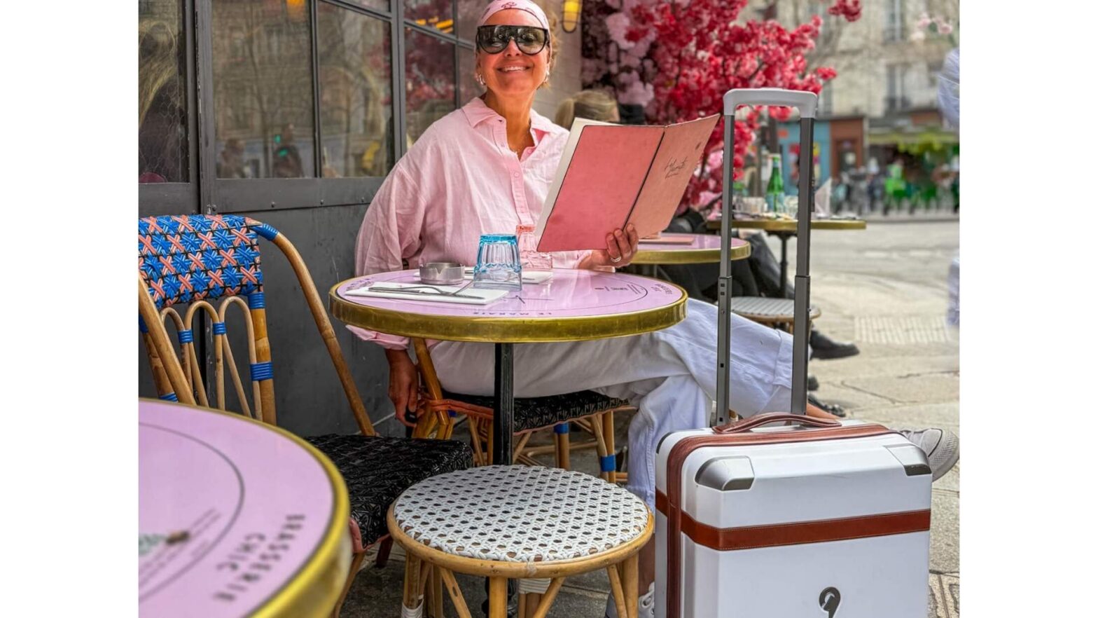 Smilende dame på kafé i Paris med hvit kabinkoffert