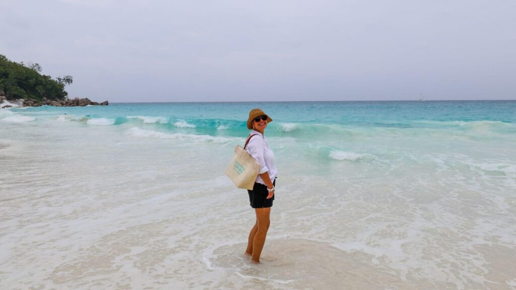 Smilende dame på strand på Seychellene omgitt av turkist hav.