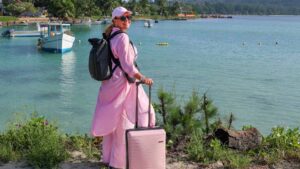 Kvinne med rosa kabinkoffert og sort ryggsekk ved sjøen på Seychellene