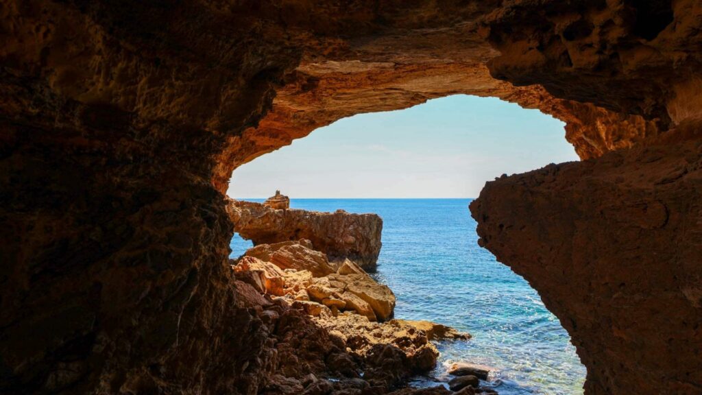 Utsikt fra Cala Comte Cave på Ibiza med klippeformasjoner, turkist hav og Middelhavet sett fra innsiden av grotten.