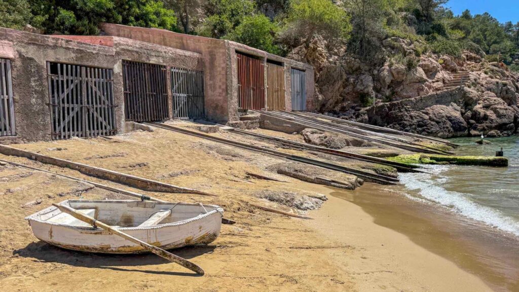 Tradisjonelle båthus og liten fiskebåt på stranden i Cala de Sant Vicent på nordkysten av Ibiza.