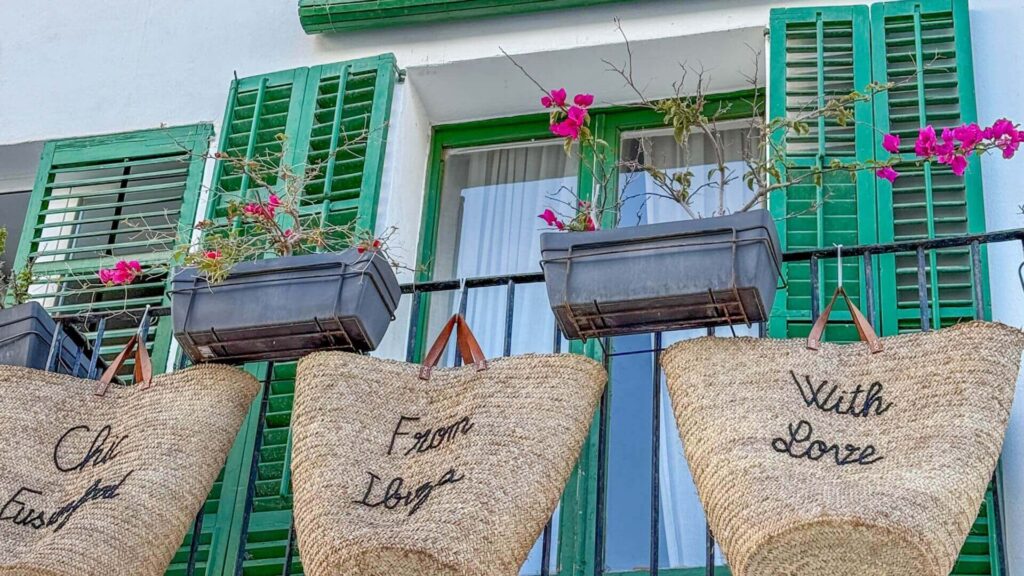 Stråvesker og grønne skodder i en liten butikkgate i Ibiza by.