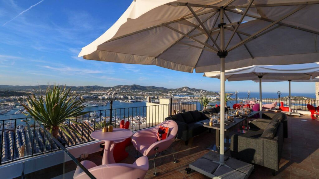 Rooftop-bar med panoramautsikt over havnen og Ibiza by ved solnedgang.