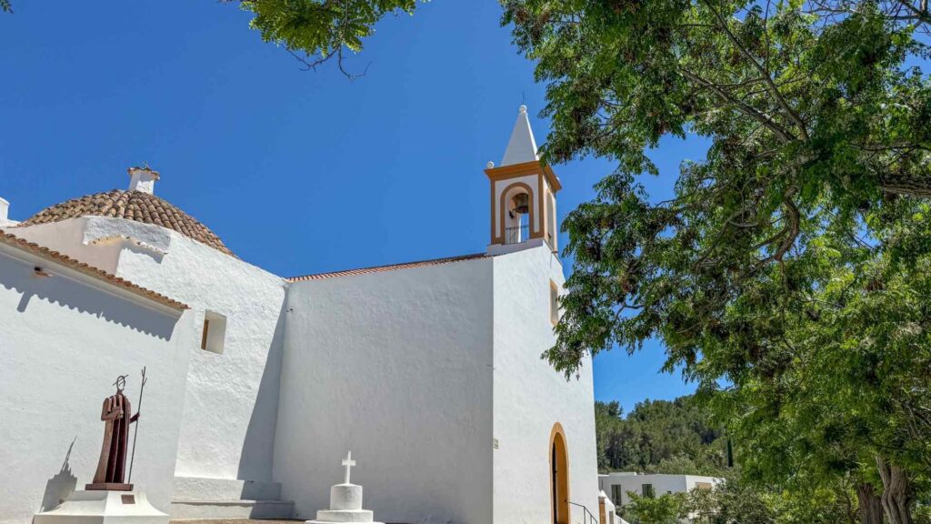 Den hvitkalkede kirken i Sant Joan de Labritja nord på Ibiza omgitt av grønt landskap og tradisjonell ibizisk arkitektur.