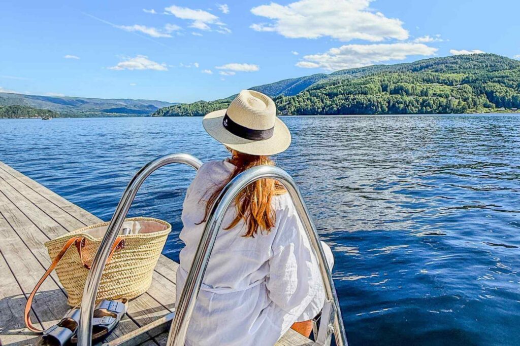 Person nyter utsikten fra brygga ved DUGG badstue i Notodden, med Heddalsvannet og skogkledde åser i bakgrunnen.