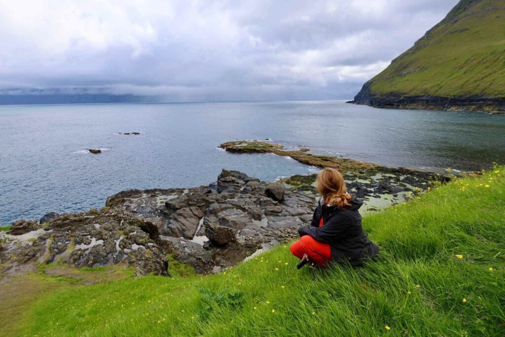 Utsikt over klippekysten og Atlanterhavet ved Gjógv på Færøyene, med en reisende som nyter landskapet.