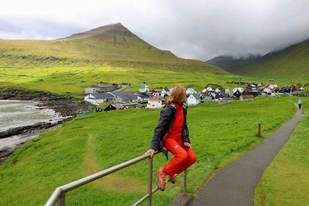 Reisende ved Gjógv på Færøyene med landsbyen, kirken og de karakteristiske fjellene i bakgrunnen.