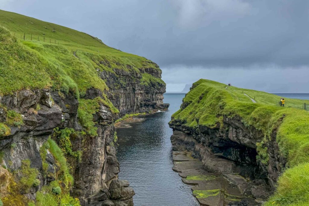 Den naturlige kløften og havnen i Gjógv på Færøyene, omgitt av bratte klipper og grønne gresskledde fjellsider.