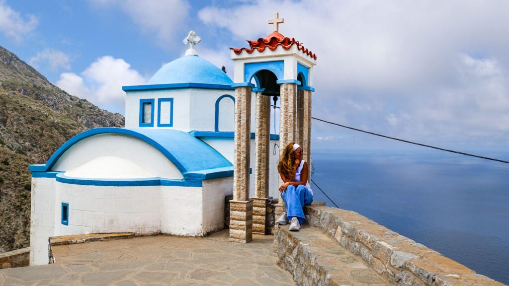 Reisende ved kirken i Olympos på Karpathos med utsikt over Egeerhavet og de dramatiske fjellene.