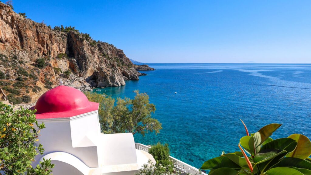 Utsikt mot Kyra Panagia-stranden på Karpathos med det ikoniske kapellet med rød kuppel og utsikt over Egeerhavet.