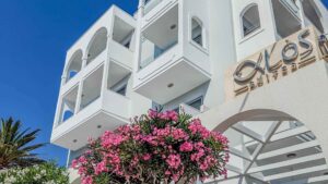 Alos Suites i Pigadia på Karpathos, hvit hotellbygning med balkonger og rosa blomster.