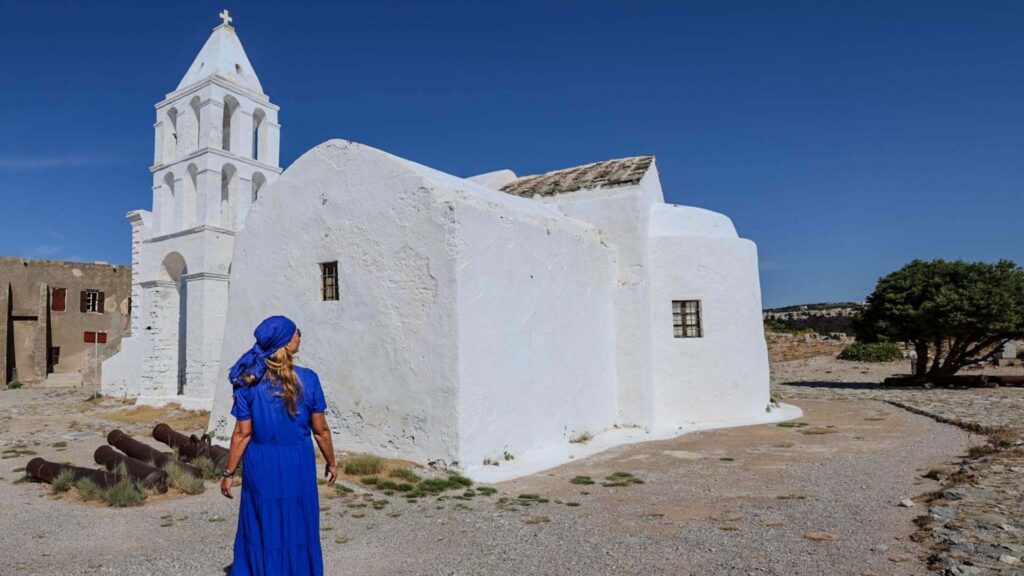 Hvitkalket gresk kirke med klokket&aring;rn i Chora  med kvinne i bl&aring; kjole foran kirken.