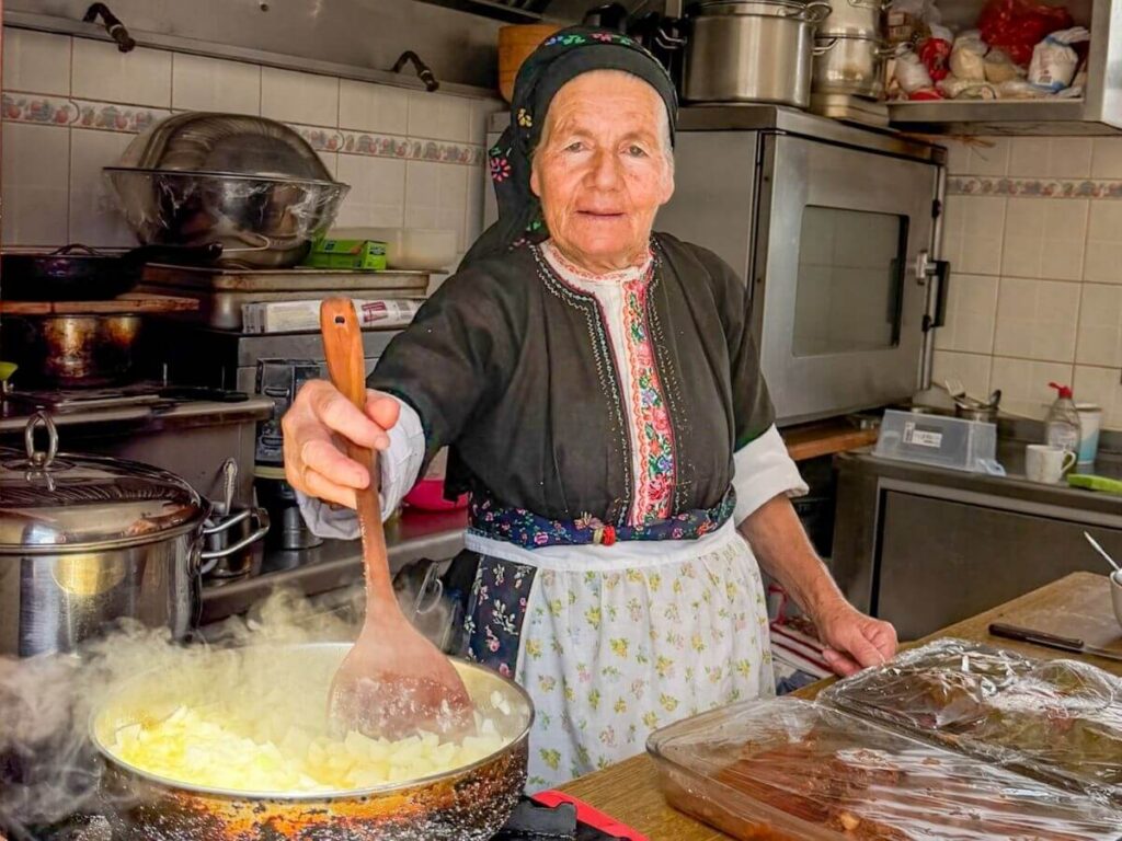 Eldre kvinne i tradisjonelle kl&aelig;r tilbereder mat i et kj&oslash;kken p&aring; Karpathos i Hellas.
